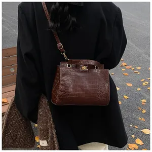Détail du sac à main marron foncé à motif crocodile avec fermoir doré sur un banc