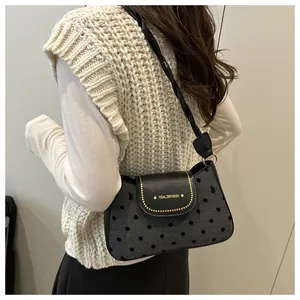Detail of shoulder bag featuring gray polka dot fabric, black leather flap and gold studs