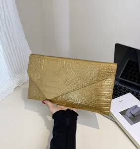 Detail view of gold envelope clutch with crocodile texture and metallic finish