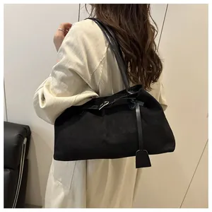 Detail of black suede tote bag with leather buckle and tag on model in white coat