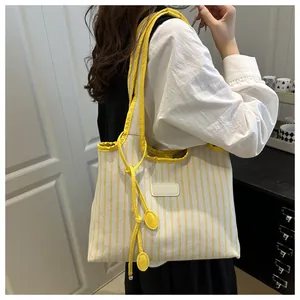 Detail of a large yellow and white striped canvas tote bag worn on shoulder by a model