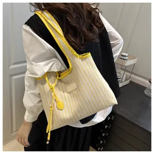 Detail of yellow and white striped canvas tote bag with long handles and side tassel