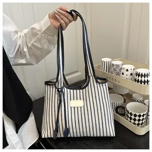 Detail of striped canvas tote bag with blue leather handles and contrast stitching