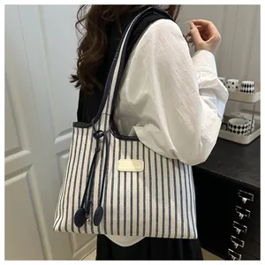Detail of blue and white striped canvas tote bag with side drawstrings and tan leather patch