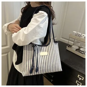 Detail of striped canvas tote bag with leather trim worn on the shoulder by a model