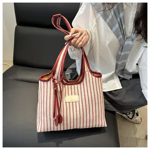 Detail of red and white striped canvas tote bag with leather handles and tassel pendant