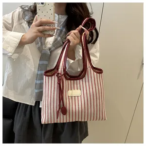 Detail of red and white striped tote bag with burgundy leather trim and shoulder strap