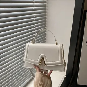 Chic white leather handbag with gold V-buckle and adjustable shoulder strap