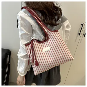 Model wearing a red and white striped fabric tote bag with dark red leather straps