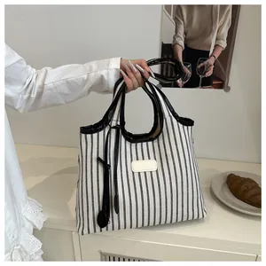Detail of striped canvas tote with black leather trim and handles in a cozy home setting