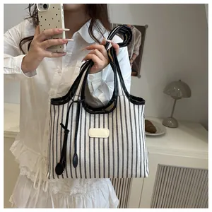 Detail of striped canvas tote bag with black leather trim and decorative charm