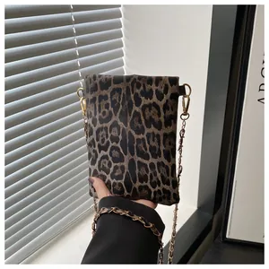 Detail of leopard print mini crossbody bag with gold chain strap held by a hand