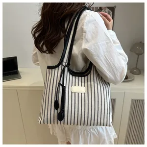 Close-up of striped canvas tote bag with leather handles and decorative pompom charm