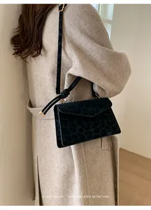 Détail du sac bandoulière noir à motif léopard avec fermoir doré porté par un mannequin