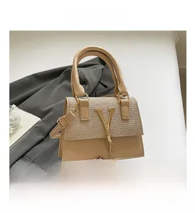 Detail view of beige crossbody bag with gold V-hardware and metallic tassel accents