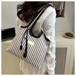 Detail of a large striped canvas tote bag with black leather trim and tassel accents