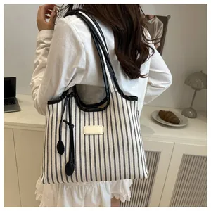 Detail of striped canvas tote bag with black leather straps and side tassel charm