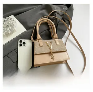 Detailed view of beige crossbody bag with gold V buckle and tassel next to a smartphone