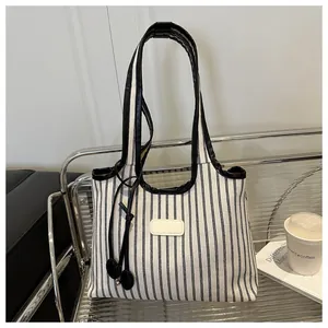 Detail of striped canvas tote bag with black leather straps on a silver metal stand