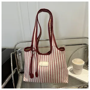 Detail of red and white striped tote bag featuring a leather tassel and leather handles