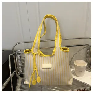 Detail of yellow striped canvas tote bag with leather tag on a modern metal shelf