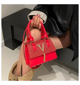 Detail of red glitter crossbody bag with gold V logo and tassel held by a model