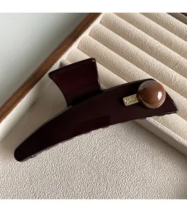 Detailed close-up of a coffee-colored hair claw clip with a glossy bead on velvet padding