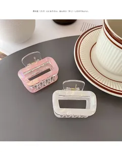 Close-up of translucent square claw clips in iridescent pink and white on a grey mat