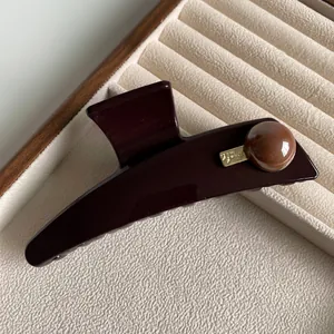 Glossy coffee brown hair claw with golden metal plate on premium wooden jewelry tray