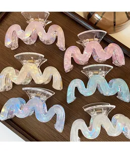 Detail of six iridescent acrylic wave hair claws on a dark wood tray with aurora finish