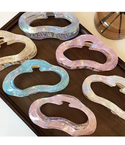 Close-up of six pearlescent cloud-shaped hair claws with aurora finish on a wooden tray