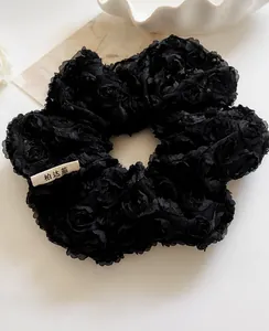 Detailed close-up of large black lace scrunchie with 3D rose floral texture and logo label