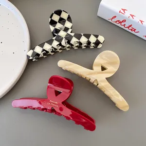 Three large acetate hair claws in checkerboard, marble, and red, shown in top view