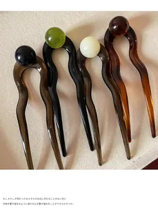 Detail of four acetate U-shaped hairpins with colorful beads on textured fabric background