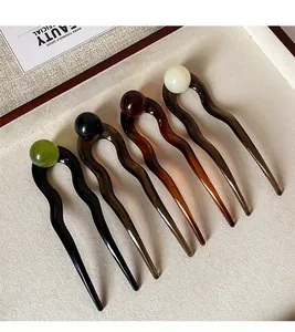 Close-up of five colorful acetate U-shaped hairpins with decorative round beads in a tray