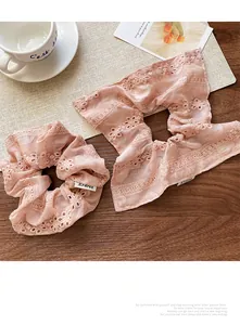 Detail of pink lace scrunchies with floral embroidery and brand label on a wooden table