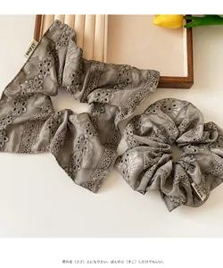 Detail of taupe lace scrunchie with floral embroidery and brand label on wooden tray