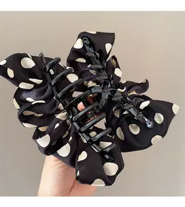 Close-up of a large black and white polka dot bow hair claw clip with silk texture details
