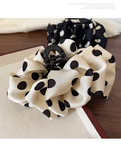 Detailed close-up of large polka dot fabric hair claw clip with silky pleated texture