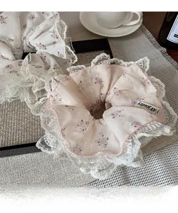 Detalle de coleteros de gasa floral con encaje blanco y etiqueta textil de la marca