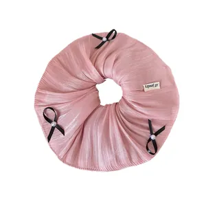 Pink satin scrunchie with pearlescent sheen and three black bows with white pearls