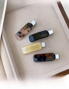 Detail of four acetate hair clips in tortoiseshell and solid colors on a beige tray