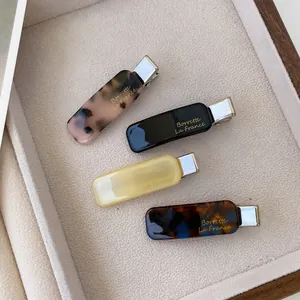 Elegant acetate duckbill hair clip set in four colors with gold logo on gray felt tray