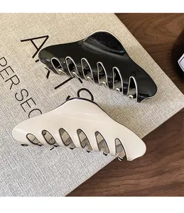 Detail of glossy black and cream French hair claws with wide curved teeth on a textured board