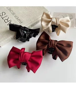 Top view of large satin bow hair claws in red, brown, beige, and black on white background