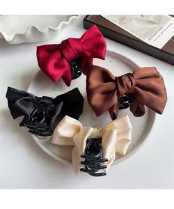 Detail of four satin bow hair claws in burgundy, coffee, black, and cream in a ceramic tray
