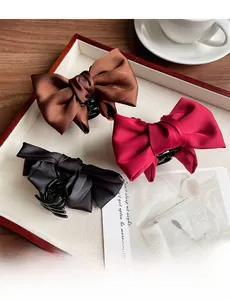 Detailed view of satin bow hair claws in brown, burgundy, and black on an elegant tray