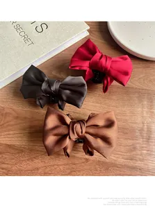 Three satin bow hair claws in red, grey, and brown displayed on a wooden table
