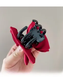 Detailed view of a large red satin bow hair claw clip with black plastic shark teeth