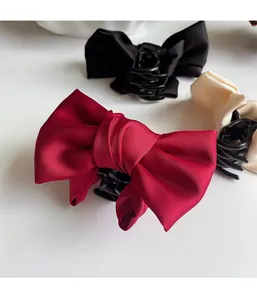 Detailed close-up of large satin bow hair claw clips in red, black and beige colors
